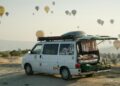 a van is parked in a field with hot air balloons in the sky