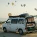 a van is parked in a field with hot air balloons in the sky